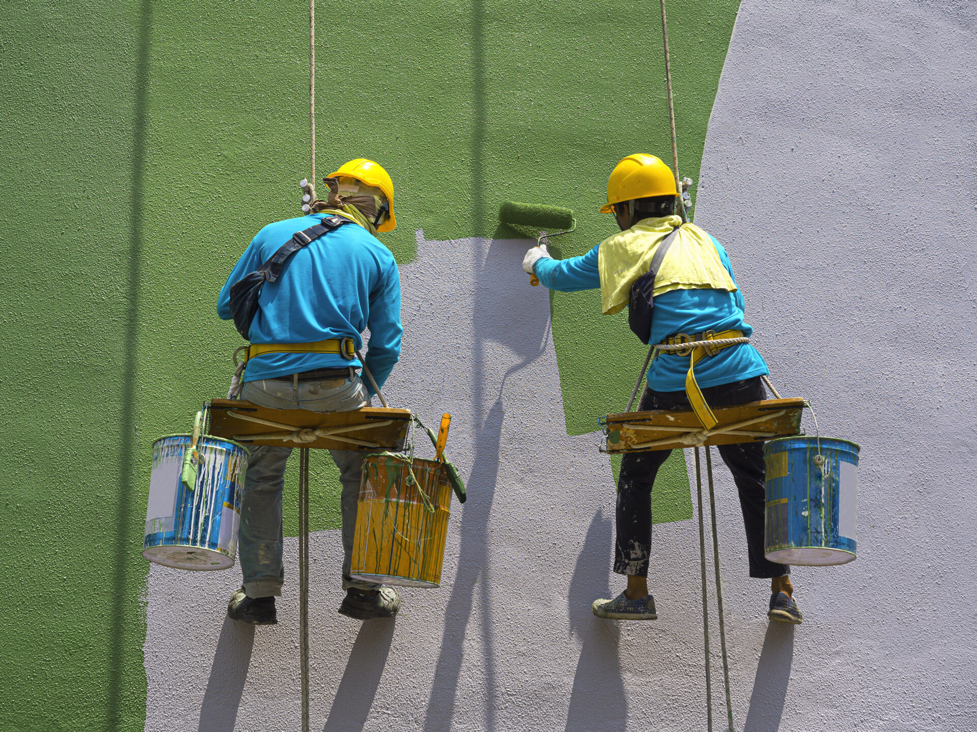 Two painters are painting the exterior of the building on a dangerous looking scaffolding hanging from a tall building.